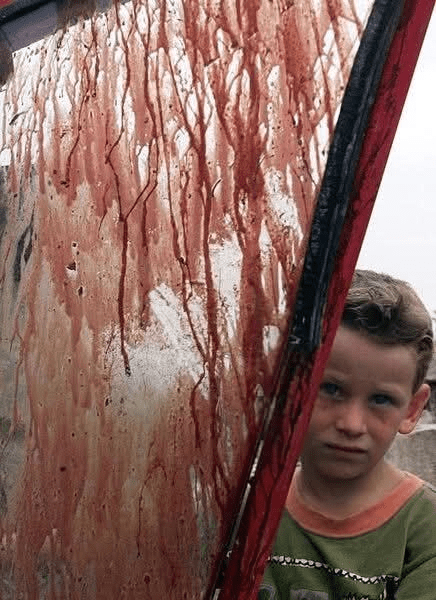 An Albanian child looks at the bloody shield of the tractor in which Serbs killed two family members, Behram and Baki.