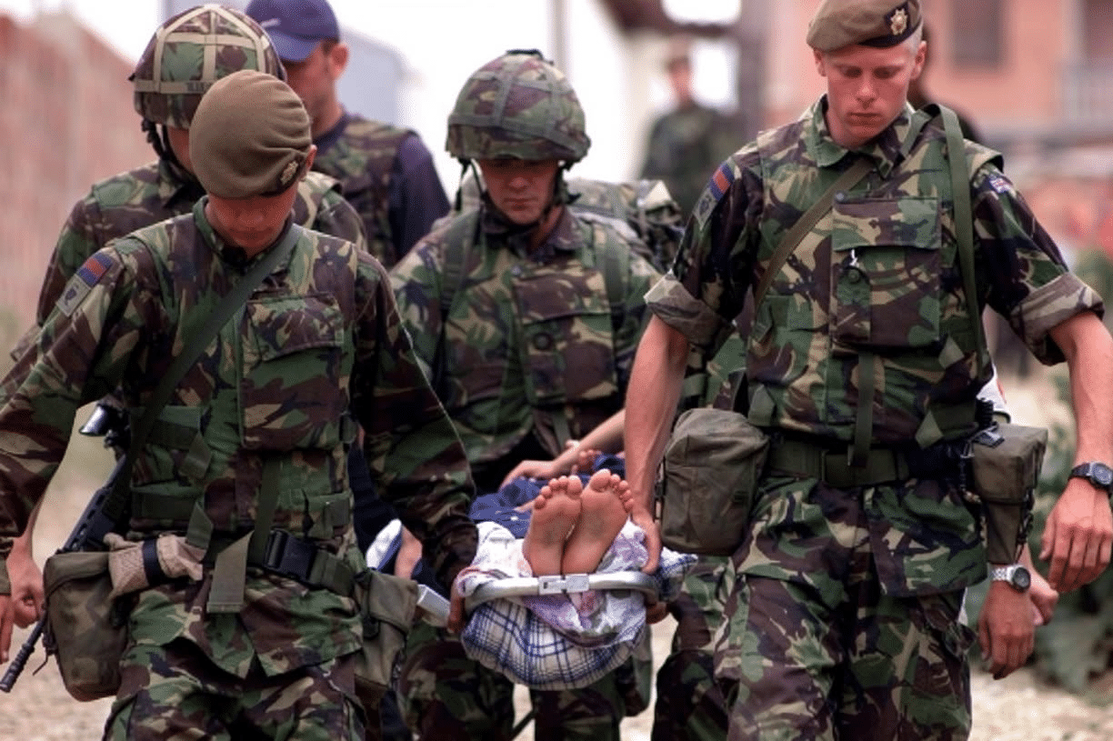 Irish Guards support an injured Albanian woman who had been raped by Serb paramilitary soldiers and thrown from a third-floor window